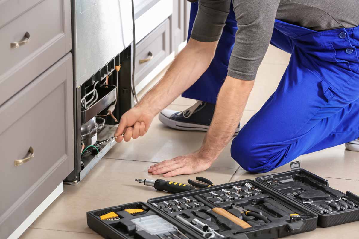 Technician kneeling to repair refrigerator